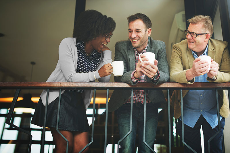 Coworkers laughing as they drink coffee while leaning over a railing